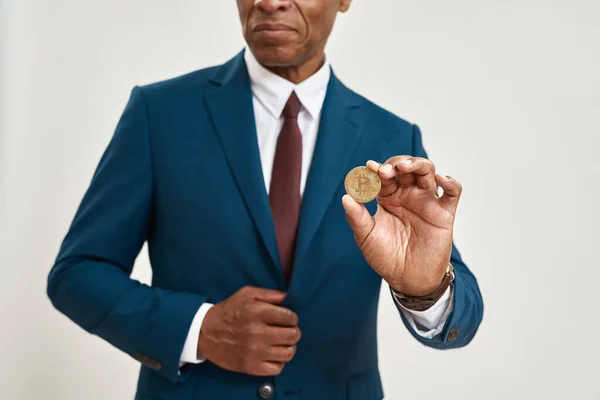 Obscure face of african american businessman holding crypto coin. Adult man wear suit. Modern successful male lifestyle. Cryptocurrency for digital payment. White background. Studio shoot. Copy space