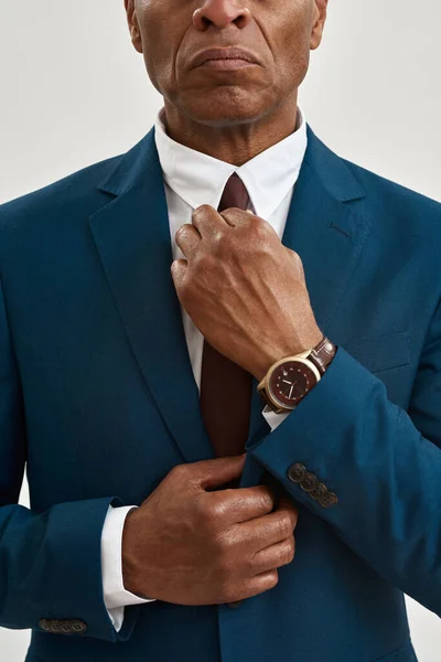 Partial image and obscure face of serious adult african american businessman straighten tie of his suit. Concept of modern successful male lifestyle. Isolated on white background. Studio shoot