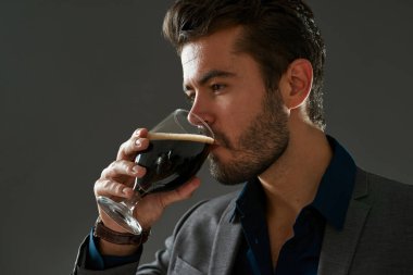 Kafkas biracı girişimcinin bir kısmı bardaktan bira içiyor. Resmi kıyafetler giyen sakallı adam. Bira işi kavramı. Bira tatma fikri mi? Stüdyodaki gri arka planda izole edilmiş. Boşluğu kopyala