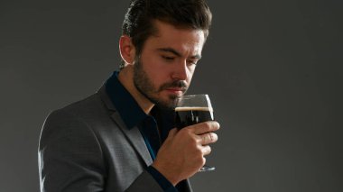 Bardakta bira koklayan Kafkas biracı girişimcinin bir kısmı. Resmi kıyafetler giyen sakallı adam. Bira işi. Bira tatma. Gri arka planda izole edilmiş. Stüdyo çekimi. Boşluğu kopyala