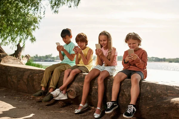 Grupo Niños Multirraciales Sentados Tronco Usando Teléfonos Inteligentes Costa Del —  Fotos de Stock