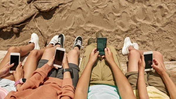 야외의 모래사장에서 통나무 위에서 아이들 스마트폰을 사용하고 띄었다 남자와 여자의 — 스톡 사진