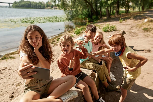 快乐的多种族孩子在沙滩的河岸玩智能手机的时候玩的很开心 一代的男孩和女孩阿尔法 小工具上瘾 童年的生活方式阳光灿烂的夏日 — 图库照片