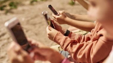 Bulanık arkadaşlarıyla açık havada cep telefonu kullanan kısmi seçici bir kız. Alfa neslinin çocukları. Gadget bağımlılığı fikri. Çocukluk yaşam tarzı konsepti. Güneşli yaz günü