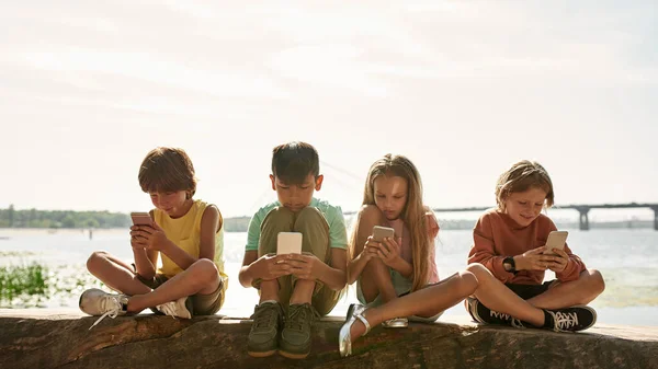Grupo Niños Multiétnicos Sentados Tronco Navegando Teléfonos Inteligentes Costa Del —  Fotos de Stock