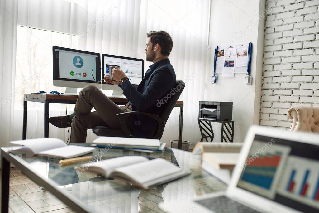 IT seller with cup of coffee speaking at video call on computer at desk in office. Online business meeting and communication. High-tech business strategy, development, promotion, selling and marketing