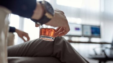 Ofisteki koltukta oturan ve dinlenen kısmen bulanık bilişim girişimcisinin elinde konyak ya da brendi bulunan seçici cam odağı. Modern başarılı erkek yaşam tarzı. Takım elbiseli ve kol saati takan adam.