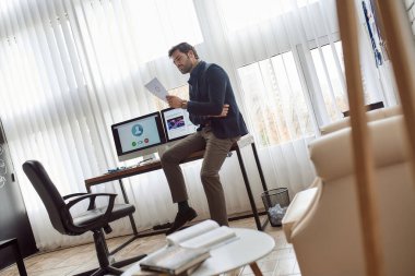 Kafkasyalı bilişim yatırımcısı büroda video görüşmesi yaparken kağıt döküman okuyor. Çevrimiçi toplantı ve iletişim. Yüksek teknoloji şirketinin iş stratejisi, geliştirilmesi, tanıtımı ve satışı