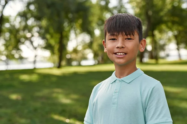 Усміхнений Багатоетнічний Хлопчик Дивиться Камеру Зеленому Газоні Розмитому Парку Відкритому — стокове фото