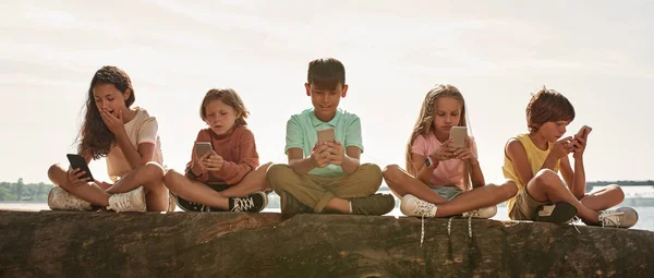 Grupo Niños Emocionales Multirraciales Sentados Tronco Viendo Teléfonos Inteligentes Costa —  Fotos de Stock