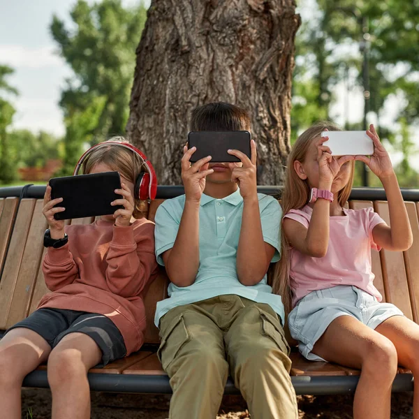 Grupo Niños Que Utilizan Navegan Teléfonos Inteligentes Banco Madera Parque —  Fotos de Stock