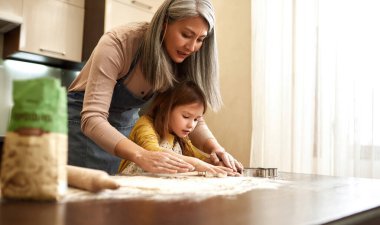 Avrupalı küçük kız büyükannesiyle kurabiye pişirmek için hamur kalıbı kullanıyor. Aile eğitimi ve birlikte zaman geçirme kavramı. Ev yapımı yemek. Ev mutfağındaki akrabalar.