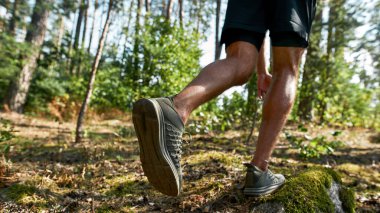 Bulanık yeşil ormanda koşan ya da koşan genç sporcunun kısmen aşağı bakışı. Spor giyim ve spor ayakkabı giyen yakışıklı bir adam. Modern sağlıklı yaşam tarzı kavramı. Güneşli yaz günü
