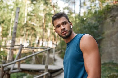 Odaklanmış, beyaz tenli bir sporcu dışarı bakıyor. Spor giyim ve kablosuz kulaklık takan yakışıklı sakallı adam. Modern sağlıklı yaşam tarzı kavramı. Sıcak yaz gündüz vakti