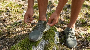 Ayakkabı bağcıklarını yosunla taşa bağlayan genç bir sporcunun kısmi görüntüsü. Atletik adam ormanda koşuyor ya da koşuyor. Modern sağlıklı yaşam tarzı kavramı. Güneşli yaz gündüz