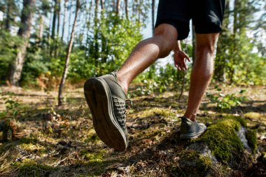 Bulanık yeşil ormanda koşan ya da koşan genç sporcunun görüntüsü kesilmiş. Spor giyim ve spor ayakkabı giyen yakışıklı bir adam. Modern sağlıklı yaşam tarzı kavramı. Güneşli yaz günü