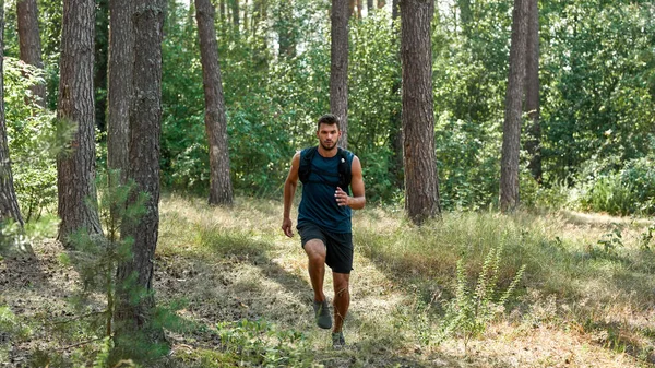 Young caucasian sportsman running or jogging in green forest. Handsome bearded dark-haired concentrated athletic man wearing sportswear. Concept of modern healthy lifestyle. Sunny summer day