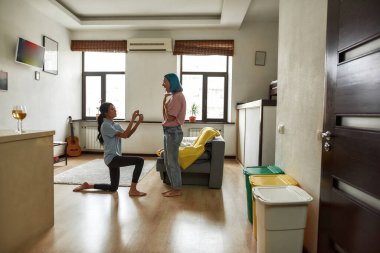 Dizlerinin üzerinde duran ve mutlu kız arkadaşına alyansını sunan kızın yan görüntüsü. Kafkasyalı genç lezbiyen çift. Evlilik teklifi ve evlilik. Romantik homoseksüel ilişki