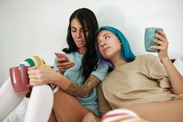 Menina Olhando Para Namorada Assistindo Smartphone Cama Jovem Casal Caucasiano — Fotografia de Stock