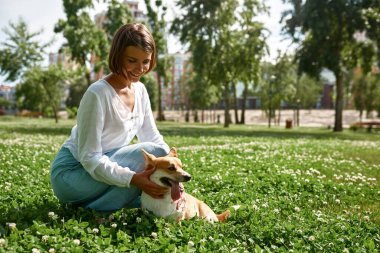 Parktaki yeşil çimlerde sevimli Corgi köpeğini okşayan beyaz bir kız. İnsan ve hayvan arasındaki ilişki kavramı. Sahiplik ve evcil hayvan arkadaşlığı fikri. Güneşli yaz günü