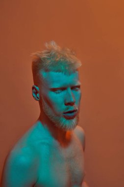Modern albino beyaz adamın kısmi görüntüsü. Gözleri kapalı. Çıplak gövdeli, genç, sakallı, Z jenerasyonunun sarışın adamı. Turuncu arka planda izole edilmiş. Stüdyo çekimi. Boşluğu kopyala