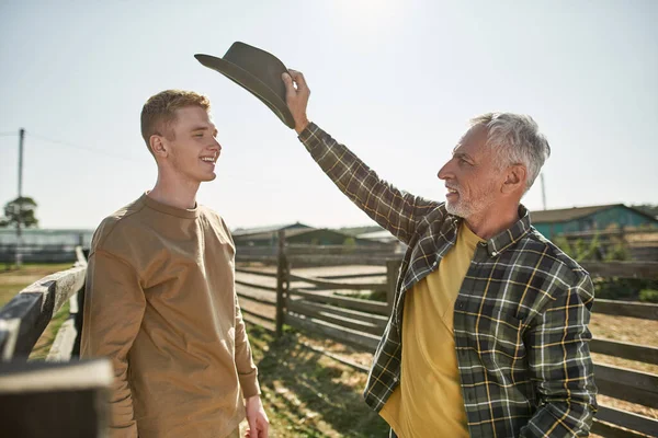 Agricultor Sênior Colocando Chapéu Cabeça Seu Neto Adolescente Sorridente Fazenda — Fotografia de Stock