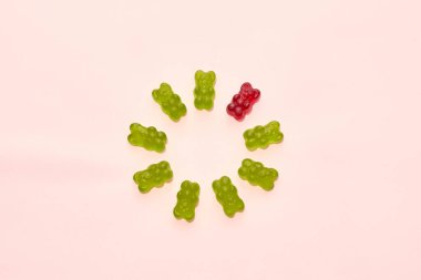 Top view of set of green and one red sweet yummy teddy bear candies in circle isolated on beige background. Dessert food for children. Confectionery. Copy space
