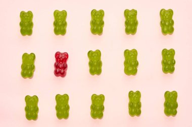 Top view of set of green and one red sweet yummy teddy bear candies in three rows isolated on beige background. Dessert food for kids. Confectionery