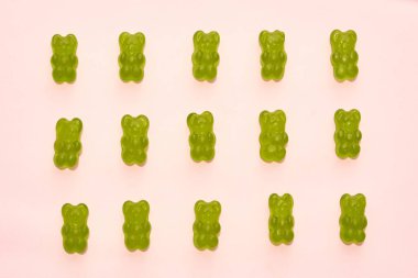 Top view of collection of green sweet yummy teddy bear candies in three rows isolated on beige background. Dessert food for kids. Confectionery