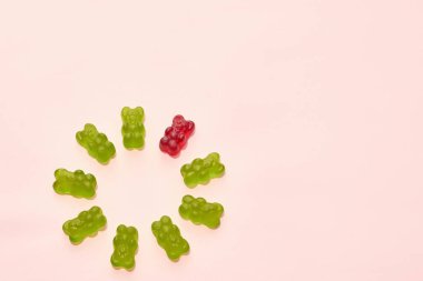 Top view of collection of green and one red sweet tasty teddy bear candies in circle isolated on beige background. Dessert food for kids. Confectionery. Copy space