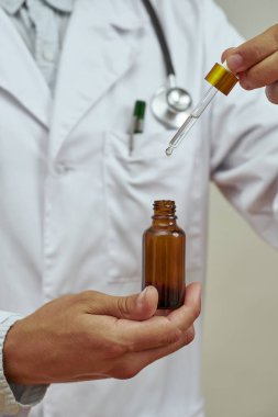 Erkek doktorun yağlı şişeden damlatıcıyı aldığı görüntüler. Steteskoplu beyaz önlüklü bir adam. Tıp ve sağlık hizmetleri kavramı. Stüdyo çekimi. Beyaz arkaplanda izole