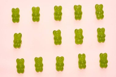 Top view of set of green sweet yummy teddy bear candies in three rows isolated on beige background. Dessert food for children. Confectionery. Copy space