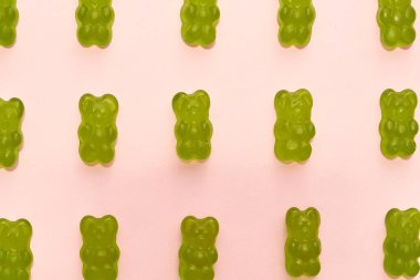 Cropped image of set of green sweet delicious teddy bear candies in rows isolated on beige background. Dessert food for children. Confectionery. Top view