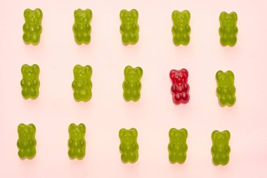 Top view of collection of green and one red sweet delicious teddy bear candies in three rows isolated on beige background. Dessert food for children. Confectionery