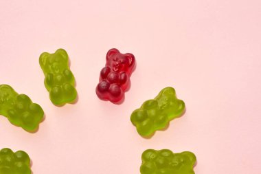 Cropped image of collection of green and one red sweet yummy teddy bear candies in circle isolated on beige background. Dessert food for kids. Confectionery. Top view. Copy space