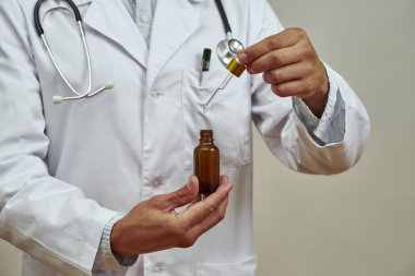 Erkek doktorun ilaç yağıyla şişeden damlatıcıyı aldığı kısmi görüntü. Steteskoplu beyaz önlüklü bir adam. Tıp ve sağlık hizmetleri kavramı. Stüdyo çekimi. Beyaz arkaplanda izole