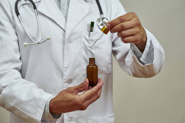 Частичное изображение мужчины-врача, берущего капельницу из бутылки с лекарственным маслом. Человек со стетоскопом в белом халате. Концепция медицины и здравоохранения. Студийные съемки Изолированный на белом фоне