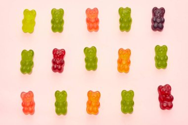 Top view of collection of colorful sweet tasty teddy bear candies in three rows isolated on beige background. Dessert food for children. Confectionery