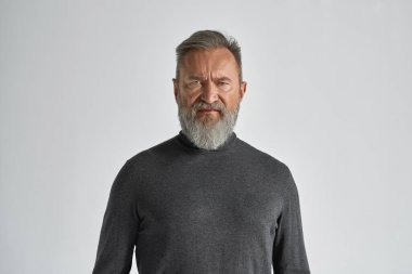 Gri saçlı, beyaz, kuşkucu yüzlü, kameraya bakan bir adam. Süveter giyen modaya uygun sakallı bir emekli. Modern yaşlı erkek yaşam tarzı. Beyaz arka plan. Stüdyo çekimi. Boşluğu kopyala