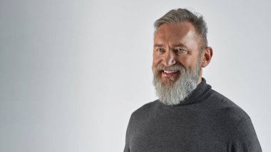 Yaşlı, gülümseyen, beyaz bir adam başka tarafa bakıyor. Sıradan kıyafetler giyen modaya uygun sakallı bir emekli. Modern son sınıf erkek yaşam tarzı kavramı. Beyaz arka planda izole edilmiş. Stüdyo çekimi. Boşluğu kopyala