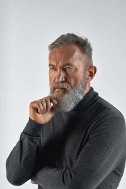 Gri saçlı, düşünceli, beyaz bir adam başka tarafa bakıyor. Süveter giyen modaya uygun sakallı bir emekli. Modern yaşlı erkek yaşam tarzı kavramı. Beyaz arka planda izole edilmiş. Stüdyo çekimi. Boşluğu kopyala
