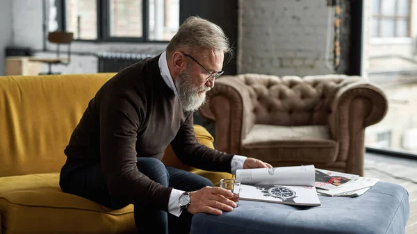 Senior Focused Caucasian Man Drinking Whiskey Reading Journal Sofa Spacious — Foto Stock