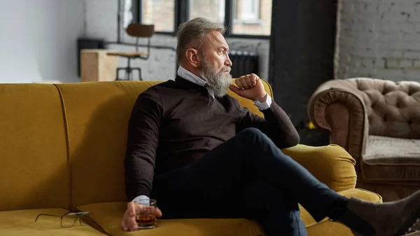 Senior Thoughtful Caucasian Man Drinking Whiskey Looking Away Sofa Spacious — Stockfoto