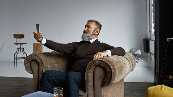 Senior Smiling Caucasian Man Taking Selfie Smartphone Armchair Spacious Apartment — Stockfoto