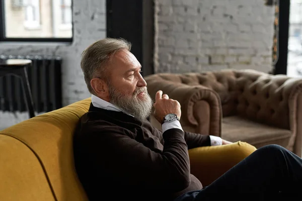 Elderly Caucasian Man Sitting Sofa Thinking Something Spacious Apartment Trendy — Stockfoto