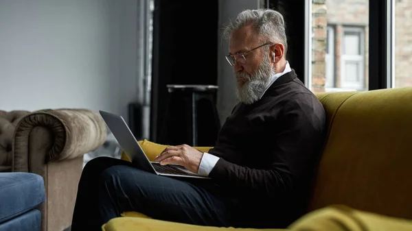 Senior Caucasian Man Typing Laptop Sofa Spacious Apartment Stylish Bearded — Stock Photo, Image