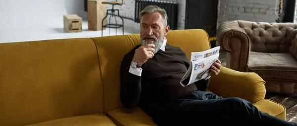 Elderly Thoughtful Caucasian Man Drinking Brandy Reading Newspaper Sofa Spacious — Stockfoto