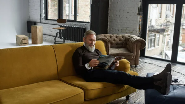 Grey Hair Concentrated Caucasian Man Reading Journal Sofa Home Fashionable — Stockfoto