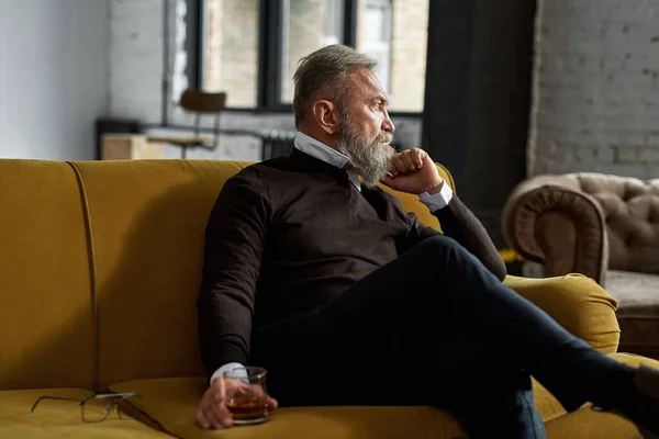 Elderly Thoughtful Caucasian Man Drinking Cognac Looking Away Sofa Spacious — Fotografia de Stock