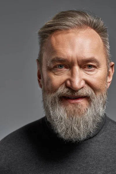 Portrait of smiling grey hair caucasian man looking at camera. Fashionable bearded pensioner wearing sweater. Concept of modern elderly male lifestyle. Isolated on grey background. Studio shoot